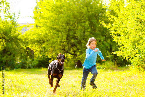 boy running away from dog or doberman in summer park © Kostiantyn