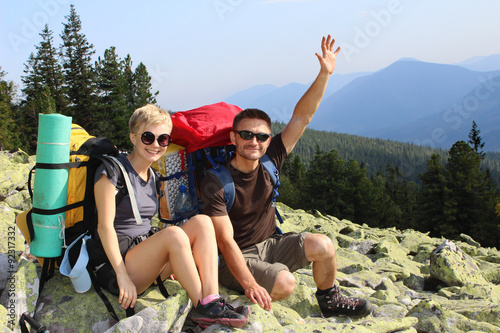 Two smiling hikers relaxing on the rock in mountains