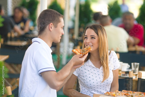 Young man feeding his beautiful girlfriend with a slice of pizza