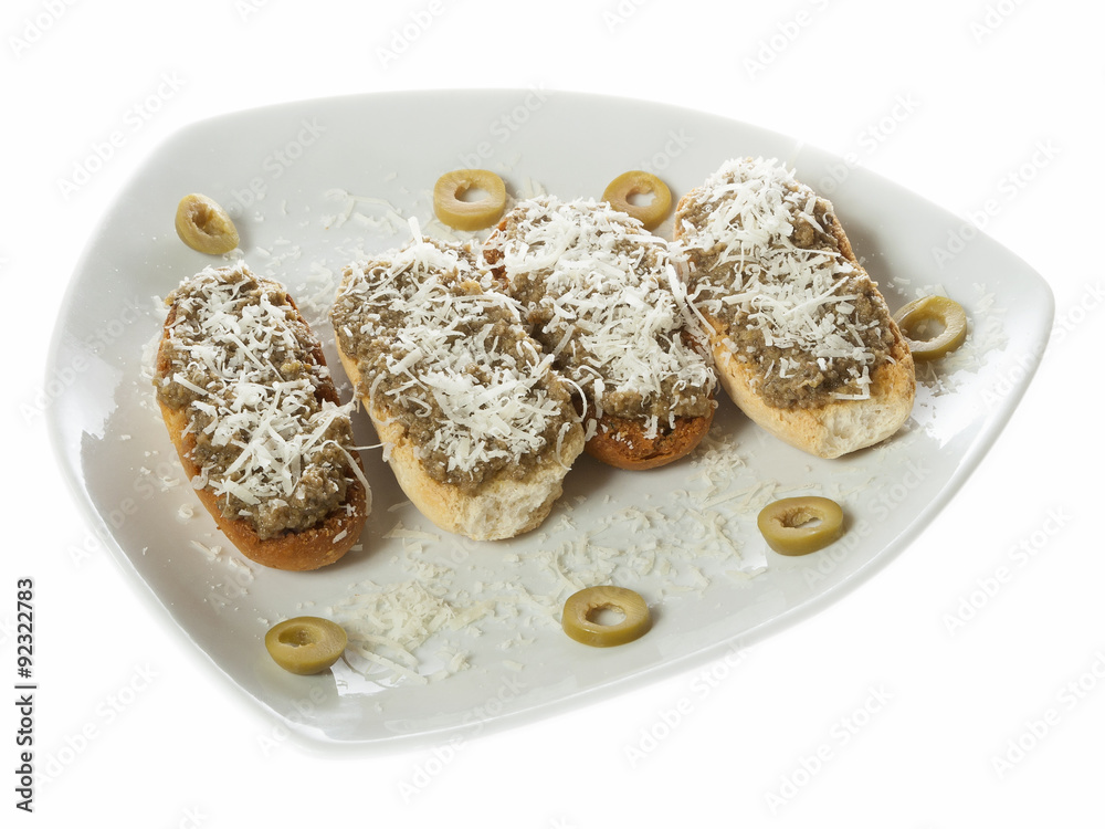 Four bruschetti with olives pate and grated cheese served on a white plate. Isolated on white.