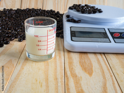 Coffee beans, measuring cup of fresh milk and dIgital balance Scale on wooden board