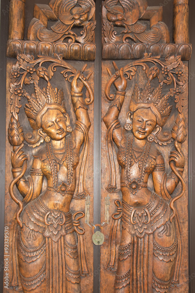 A vintage brass keyhole and religious ornament on an old exotic brown ornate Hindu temple door.