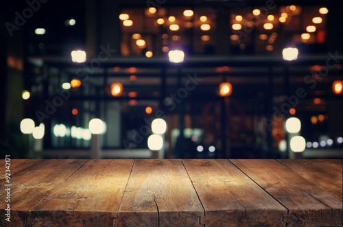 image of wooden table in front of abstract blurred background of resturant lights 