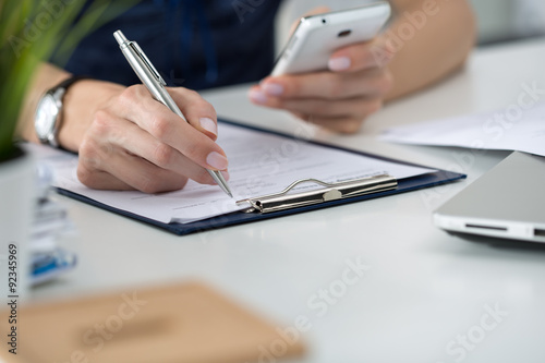 Woman writting something and looking at mobile phone
