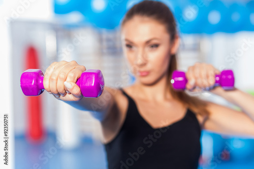 Portrait of a young pretty woman holding weights (dumbbell) in a gym.
