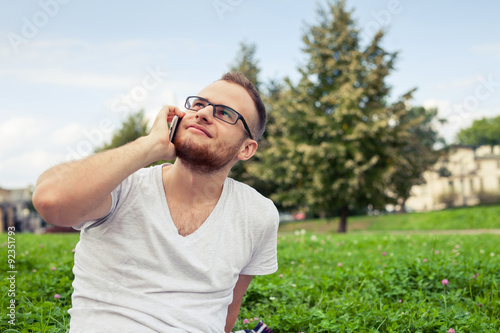 Bearded man sitting in park on blanket. He is using mobile phone.