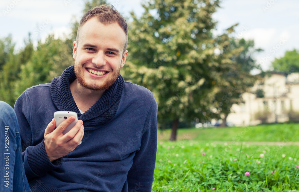 Bearded man sitting in park on blanket. He is using mobile phone. Bearded man sitting in park on blanket. He is using mobile phone.