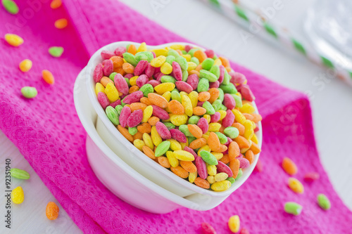 Colorful Rice Cereal on the pink dishcloth with glass of water and straws. Dishes in the shape of heart full with pink, orange, yellow and green rice