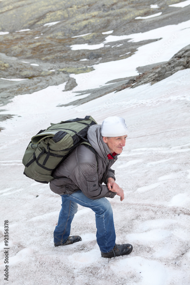 Mature Caucasian climber standing on the slippery steep slope of mountain and looking far away
