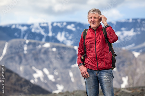 Mature hiker talking on mobile phone and looking at camera on high of mountains