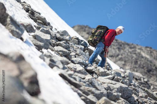 Mature man climbing in mountain at summer season, resting on steep slope