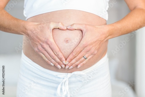 Midsection of woman making heart on belly