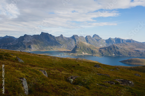 Beautiful Vibrant Norwegian Mountain Landscape from Ryten peak - famous mountain in Lofoten Islands, Moskenes municipality, Nordland with a view of Kvalvika beach, with hiking tourists and blue sky 