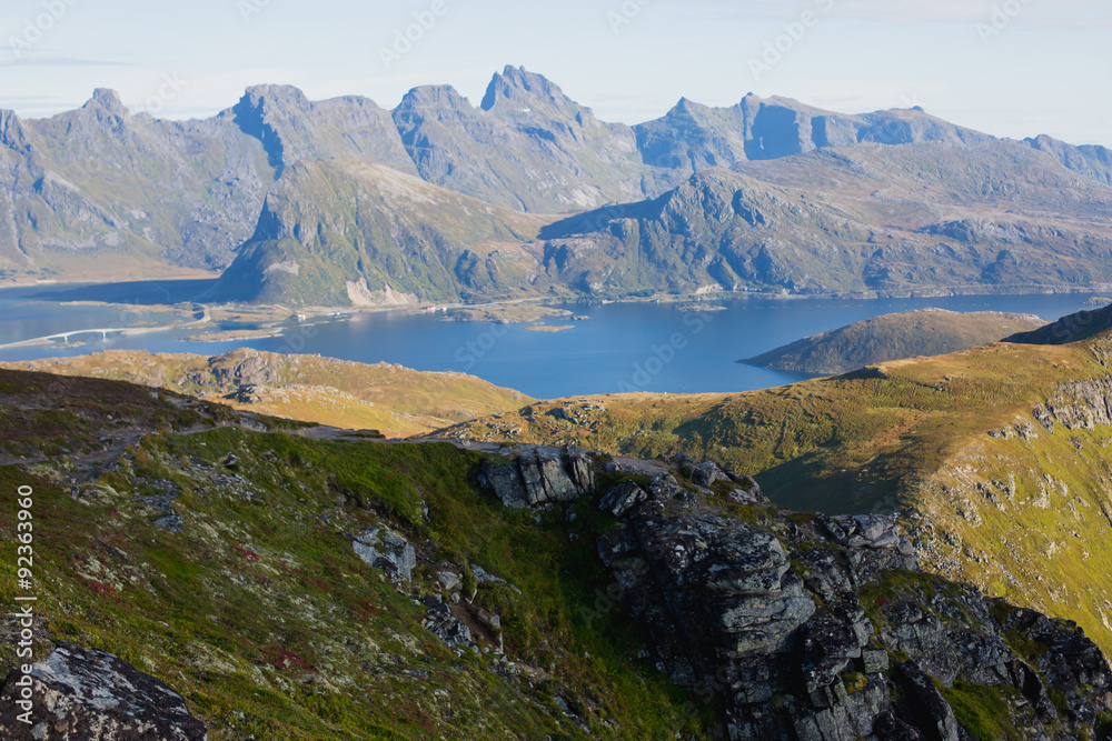 Beautiful Vibrant Norwegian Mountain Landscape from Ryten peak - famous mountain in Lofoten Islands, Moskenes municipality, Nordland with a view of Kvalvika beach, with hiking tourists and blue sky
