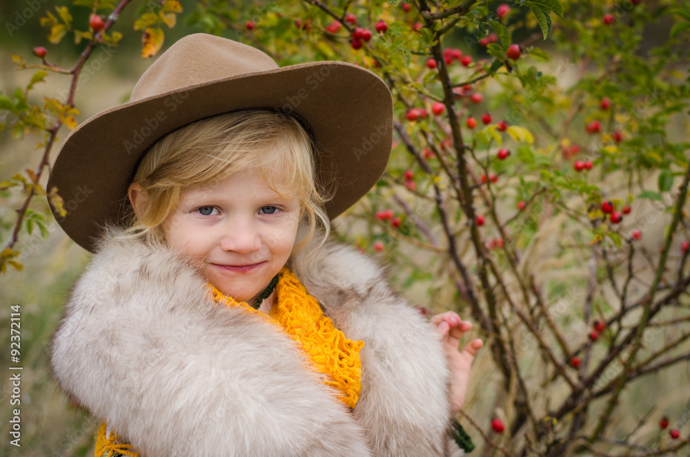 girl with hat and fur pelerine in autumn field with rose-hips