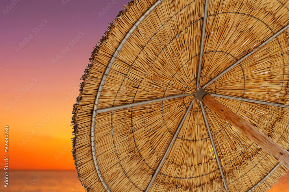 A reed sun umbrella and sun down sky symbolizing vacationing in