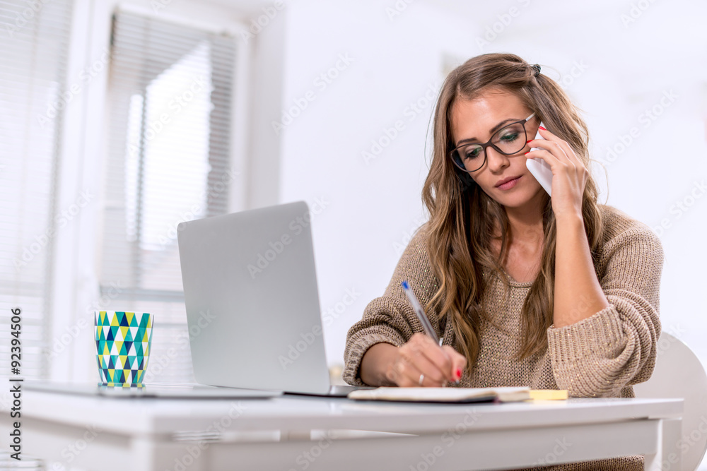 Young female writing notes while talking on phone Young female writing notes while talking on phone