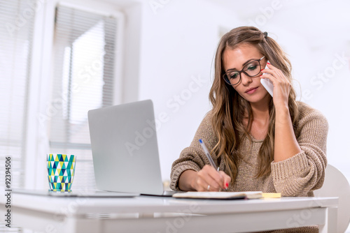 Young female writing notes while talking on phone