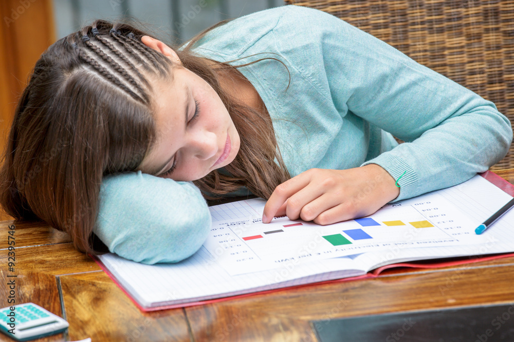 Tired or despondent young girl do homework lying on a table