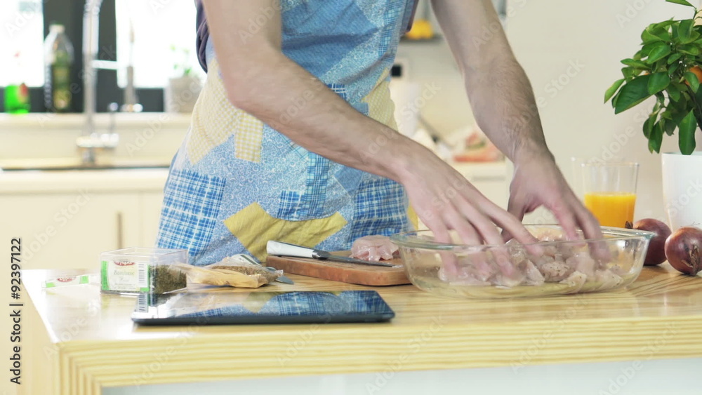 Man slicing chicken breast and searching recipe on tablet computer Man slicing chicken breast and searching recipe on tablet computer