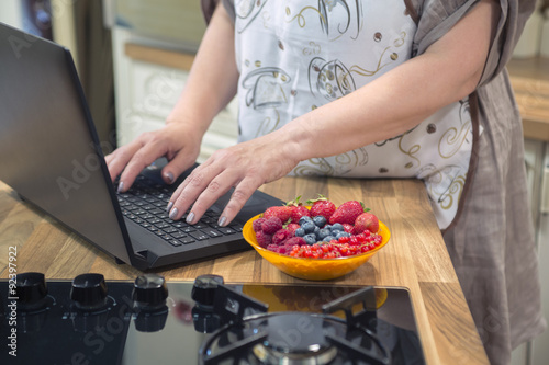Unrecognizable woman typing on laptop in the kitchen.