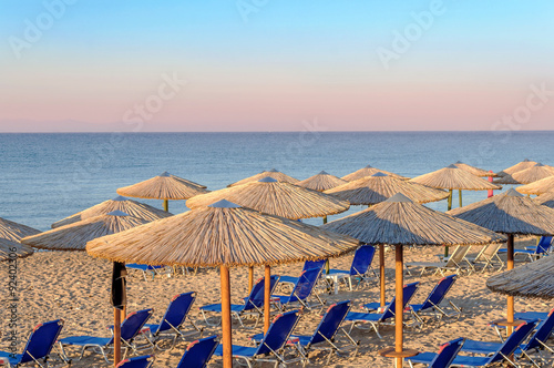 Sunbed, straw umbrella on beautiful rising sun beach background