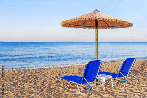Fototapeta Naklejka Na Ścianę i Meble -  Two blue sunbed, straw umbrella on beautiful beach background