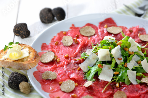 Feines Carpaccio vom Rinderfilet mit schwarzen Herbsttrüffeln und gerösteten Pinienkernen sowie Rucola mit geholbeltem  Parmesan photo