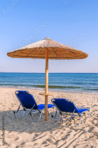 Two blue sunbed, straw umbrella on beautiful beach background in Greece 