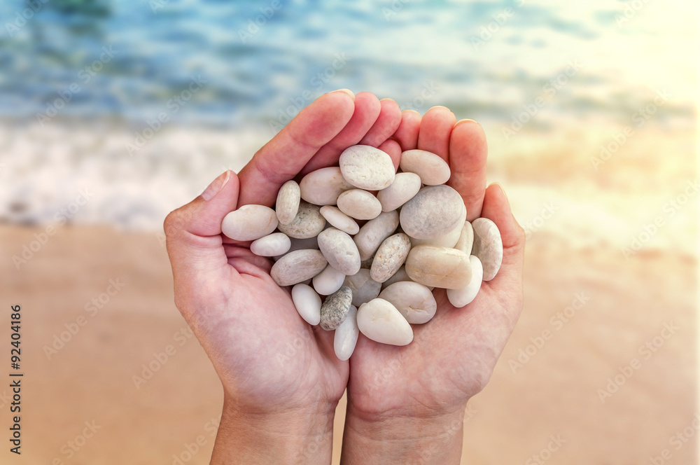 Woman hands holding small stones in hands on beach background with burning sun Woman hands holding small stones in hands on beach background with burning sun