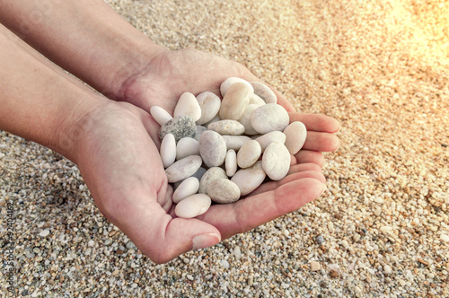 Woman hands holding small stones in hands on beach background with burning sun