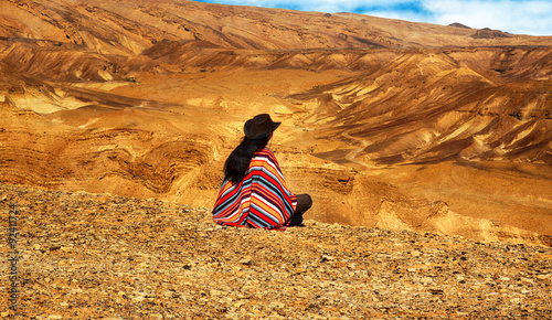 Tela Long haired man in poncho sits in a desert