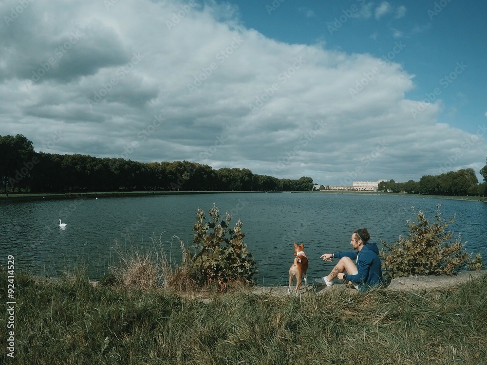man sits with his dog on the edge of Lake and pointing on swan