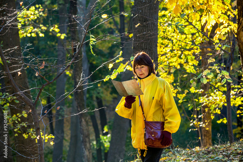 Canvas-taulu Elderly woman in yellow jacket reading old map in forest
