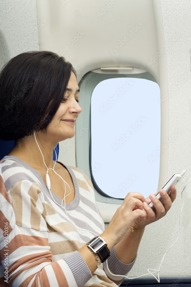Fototapeta premium caucasian woman passenger in airplane using mobile smart device with headphones