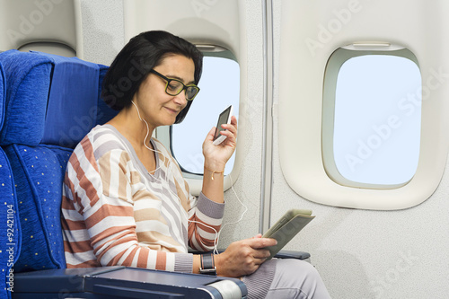 woman passenger in airplane using mobile and  tablet smart devices with headphones
