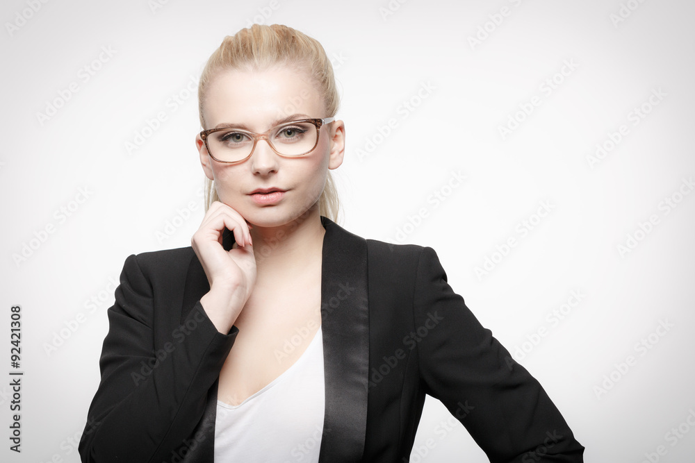 Junge hübsche blonde Mitarbeiterin im Blazer mit Lesebrille schaut souverän Junge hübsche blonde Mitarbeiterin im Blazer mit Lesebrille schaut souverän