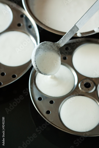 Indian idly batter poured into trays - Fresh batter being poured using a ladle into circular trays for preparing Indian Idly (Idli / rice cake) by steaming. Shallow Depth of field. Natural light used.
