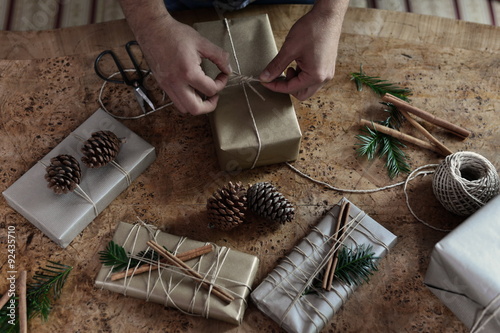 Young man wrapping his chic modern Christmas gifts presents on the wooden table