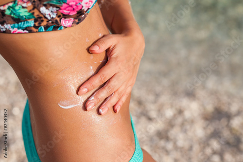 Girl standing on the beach and using suncream.