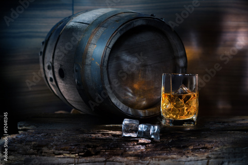 A glass of whiskey with ice on background barrel