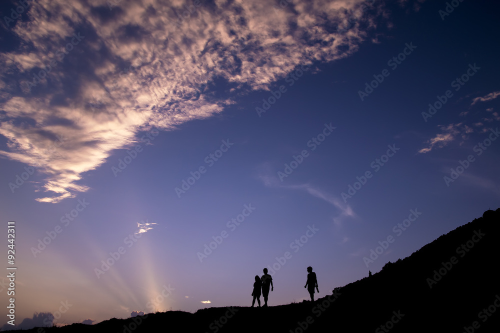Silhouette of couple and friend walking on the hill at sunset