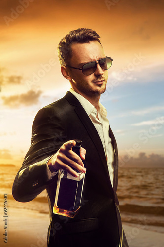 Canvas Print Attractive disheveled young man wearing elegant black suit and sunglasses holdin