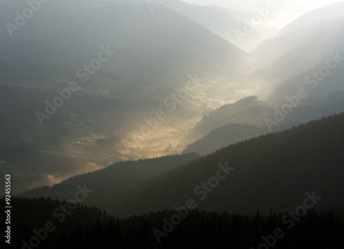 Mountain valley village in the fog and sun rays of dawn