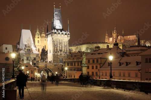 Night colorful snowy Prague gothic Castle with Bridge Tower and St. Nicholas' Cathedral and Sculptures from the Charles Bridge, Czech republic