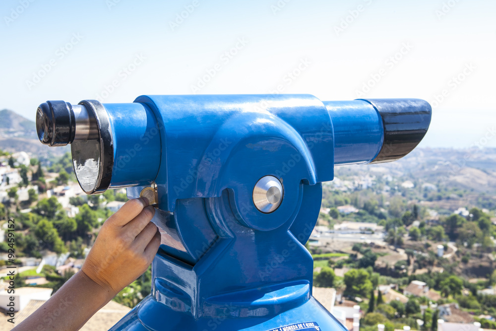 Hand inserting a coin in a blue telescope for sightseeing. Hand inserting coin.