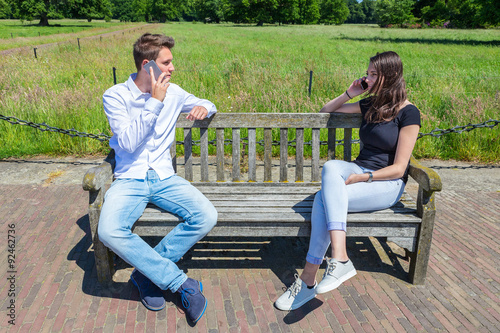 Obraz na plátně Young attractive caucasian couple calling mobile on bench in nature