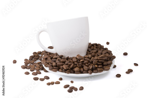 White cup on a white plate with full of roasted coffee beans.