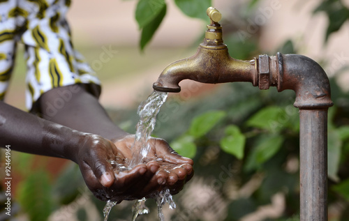 Climate Change Symbol: Handful Of Water Scarsity for Africa Symbol. Hand of an African black boy with water pouring from a tap. photo
