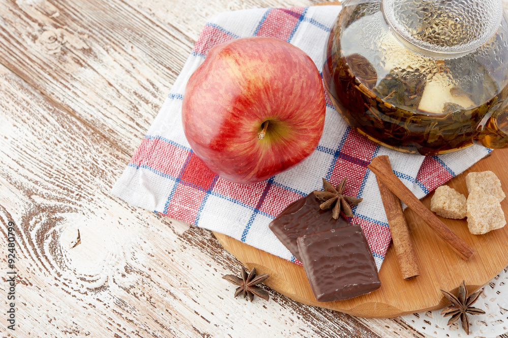 Ripe apple, cinnamon and fruit drink in glass teapot on wooden